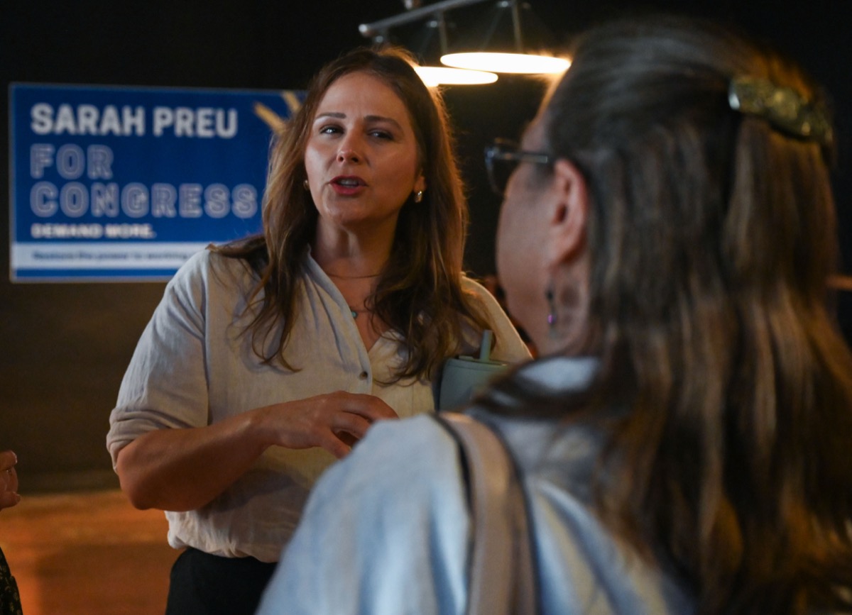 Sarah Preu talking with a supporter at a campaign event, in front of a Sarah Preu for Congress sign